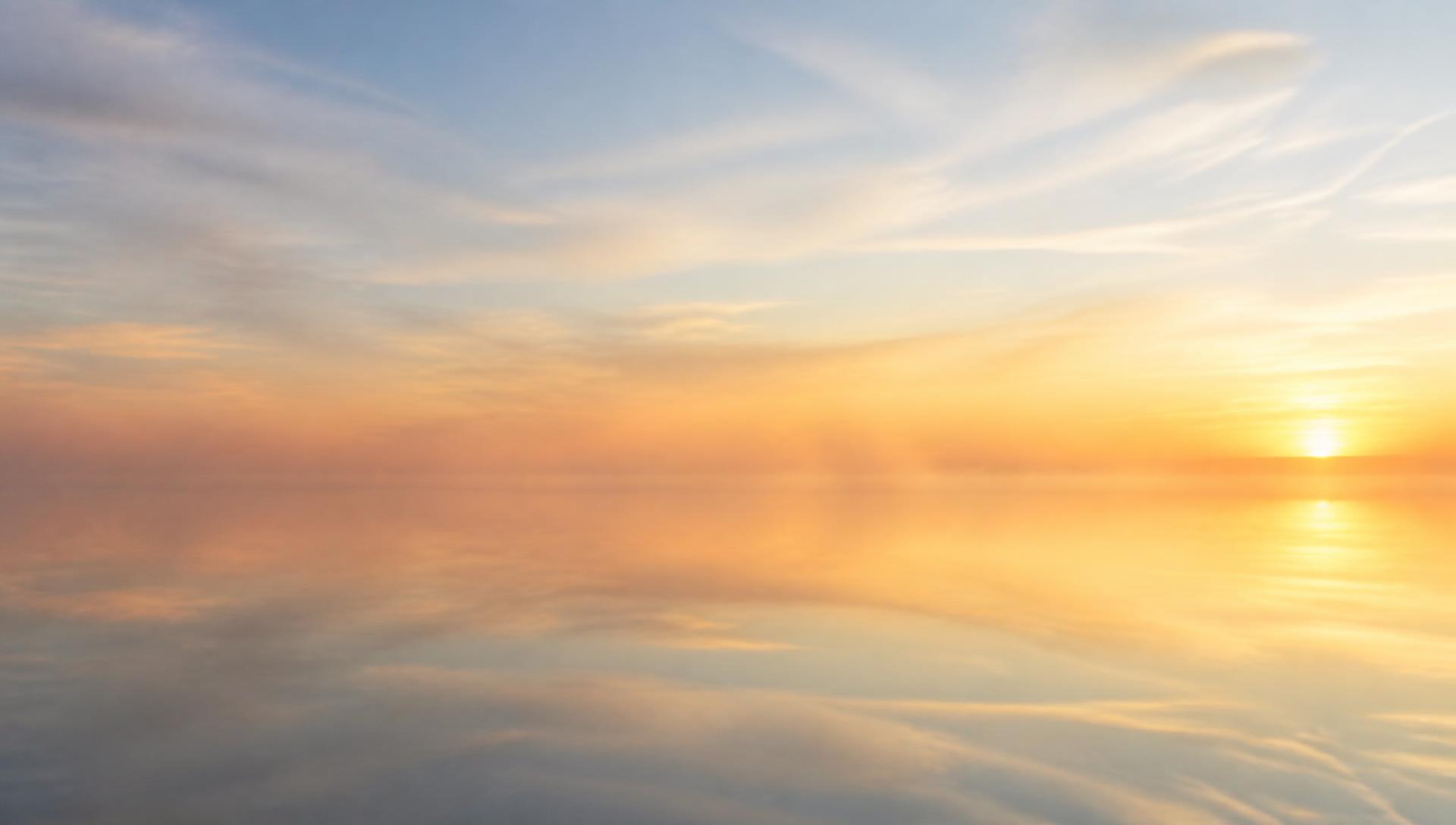 A perfectly still lake at dawn, its surface a mirror reflecting the soft morning sky, with gentle mist rising from the water